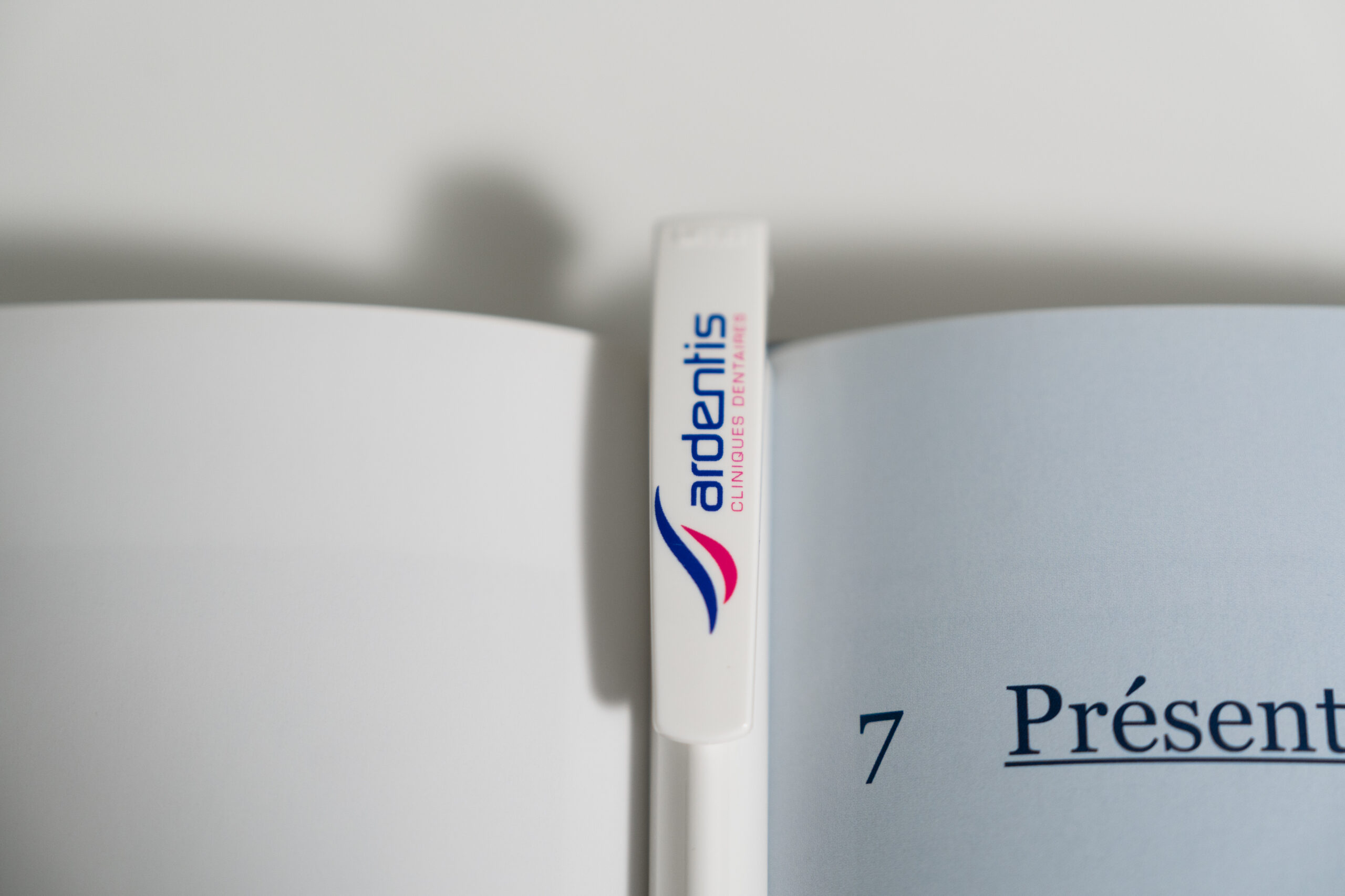 Close-up of a white Ardentis branded pen resting on an open book, highlighting office supplies and branding.
